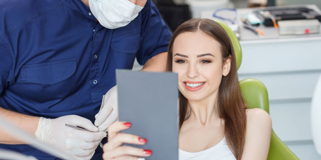 cosmetic dental patient with mirror checking out new veneers